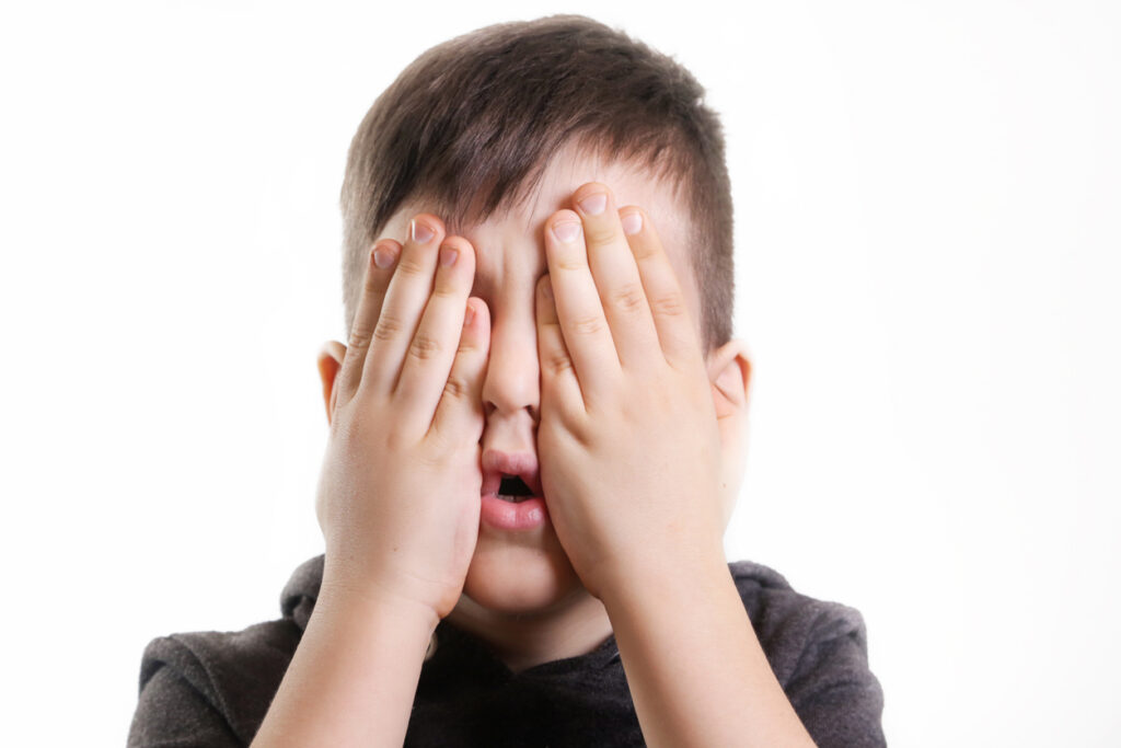 studio portrait of young boy covering his eyes see no evil concept