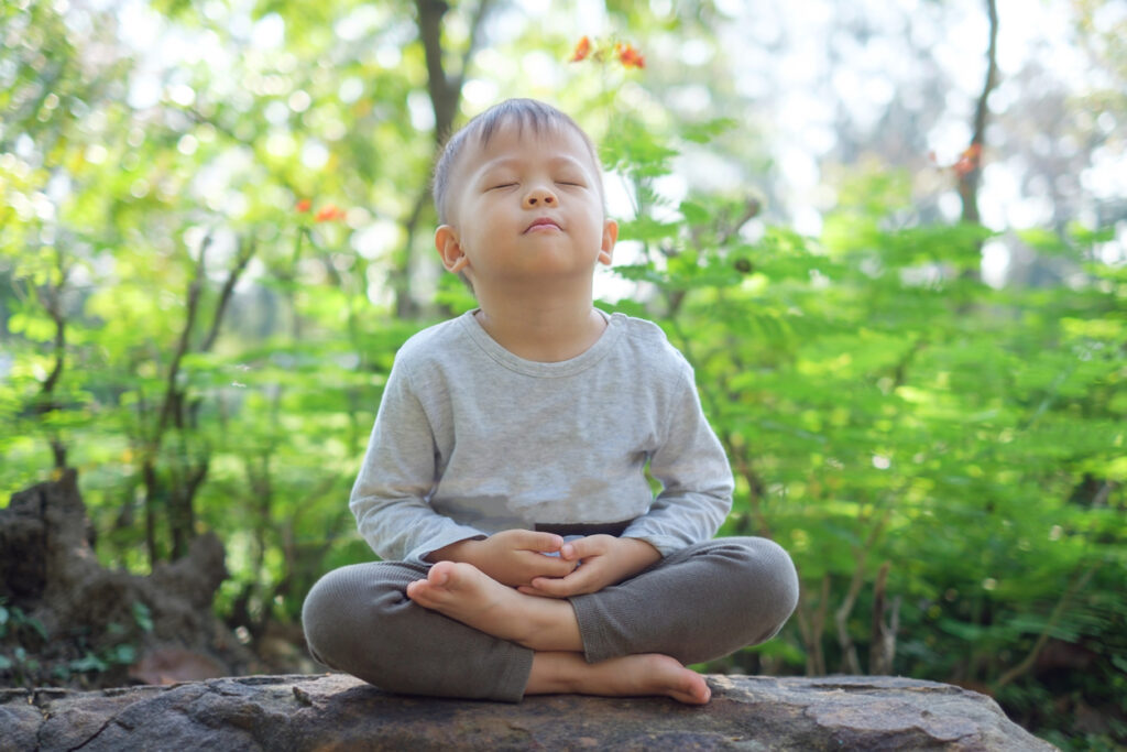 Staying Calm When Your Child Is Struggling cute little asian 2 3 years old toddler baby boy child with eyes closed, barefoot practices yoga & meditating outdoors