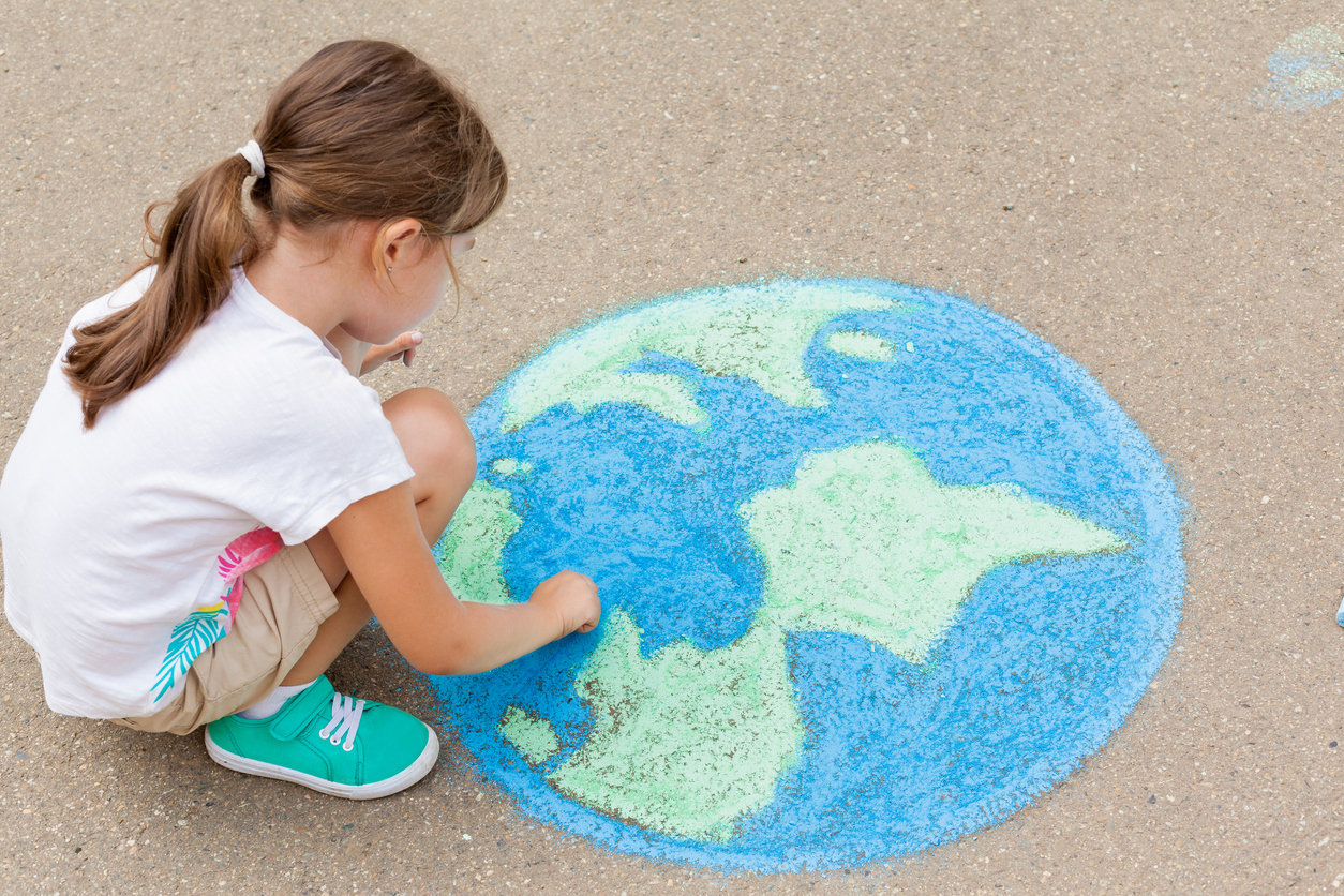 the child girl draws a planet of the world with colored chalk on the asphalt. children's drawings, paintings and concepts. education and art, be creative when you return to school. earth, peace day